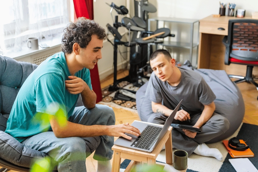 two guys living toghether and hanging out in the shared living room talking and on their computers